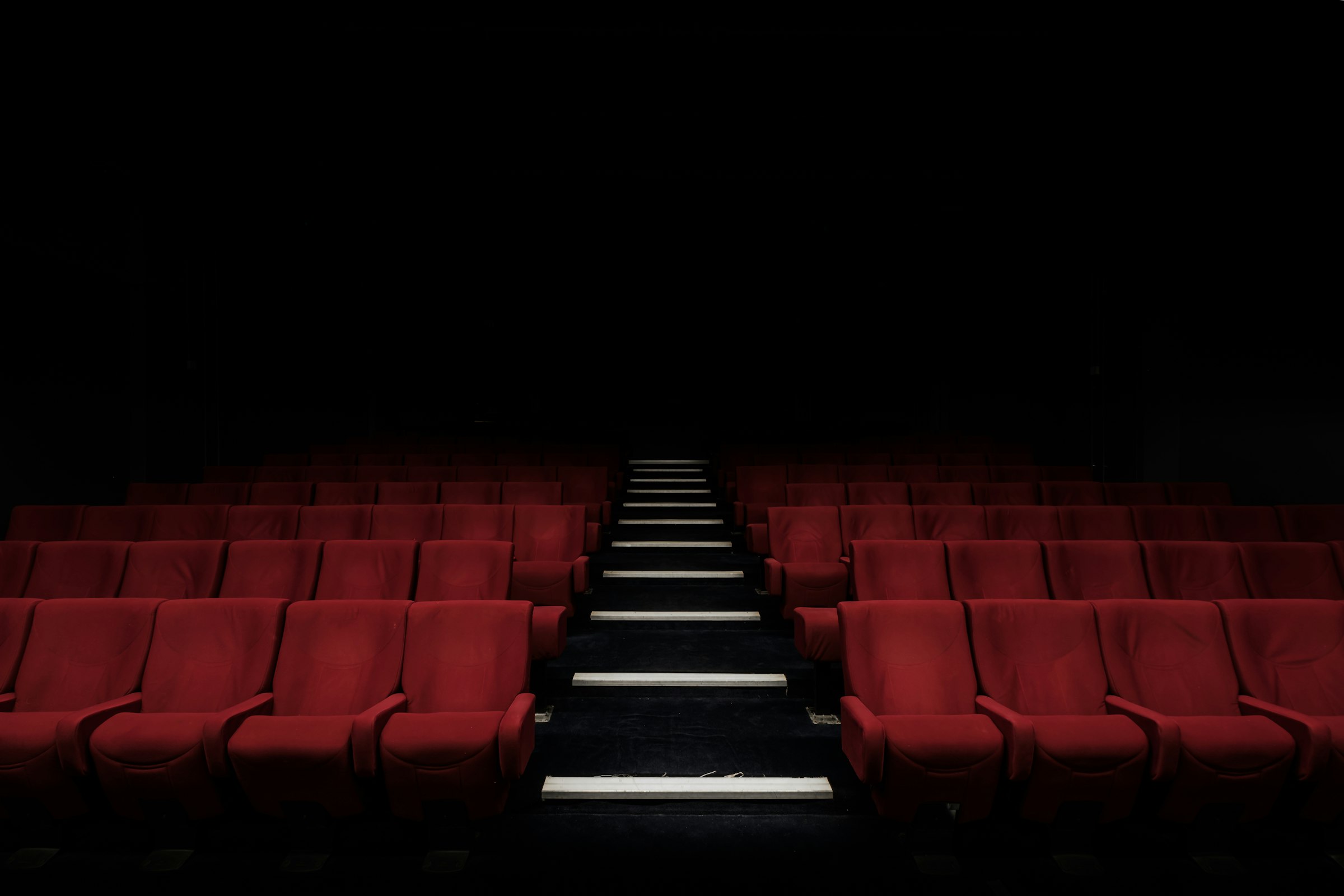 An empty theater of red seats fading into darkness — the audience that never came.